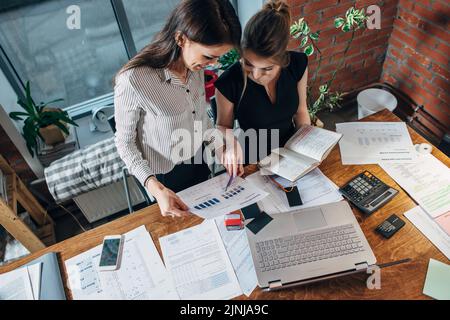 Draufsicht auf konzentrierte junge Frauen, die am Tisch sitzen und zusammenarbeiten. Stockfoto