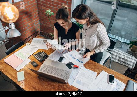 Draufsicht auf zwei weibliche Kollegen und Schreibtisch mit Papieren und Dokumenten. Geschäftsfrauen, die die Daten untersuchen und an einer neuen Vertriebsstrategie arbeiten. Stockfoto