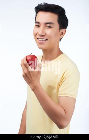 Porträt eines glücklichen vietnamesischen jungen Mannes, der einen Apfel isst Stockfoto