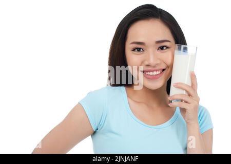 Schöne hübsche asiatische Frau, die ein Glas Milch neben ihrem Gesicht hält Stockfoto