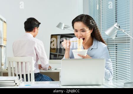 Hübsche junge Geschäftsfrau, die Ramen isst, wenn sie im Büro arbeitet Stockfoto