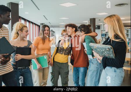 Multirassische Jugendliche Studenten umarmen in der Bibliothek Stockfoto