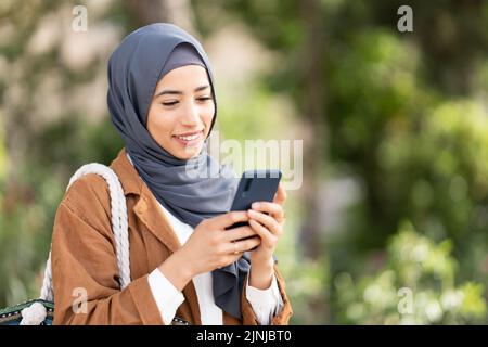 Lächelnde muslimische Frau, die ein Handy benutzt. Nahaufnahme Stockfoto