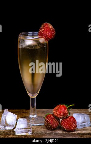 Ein vernebeltes Glas Champagner, frische Erdbeeren und Eisstücke auf dunklem Grund Stockfoto