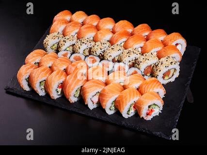 Große Sushi-Rollen, bestehend aus vielen Rollen in Kalifornien und Mackie. Sushi mit frischer Füllung auf einem schwarzen Steinteller. Stockfoto