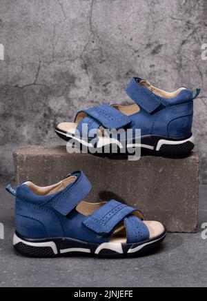 Kindermode. Zwei stylische blaue Kinder-Sport-Sandalen für Jungen auf grauem Beton-Hintergrund. Nahaufnahme eines Schuhs, der höher auf Ziegelsteinen steht Stockfoto