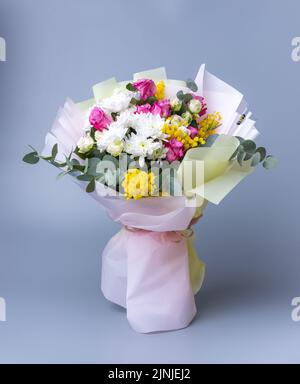 Zartes Weihnachtsstrauß, eingewickelt in helles Blumenpapier auf blauem Hintergrund. Wunderschön verpackte Blumenarrangements mit Rosen, gelben Blüten, Weißblüten Stockfoto