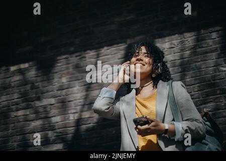 Junge Birazialfrau, die Kopfhörer trägt und Musik im Freien auf der Straße hört. Stockfoto