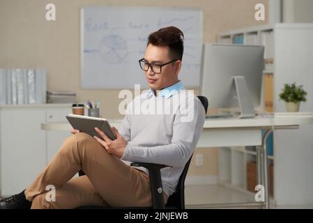 Hübscher junger Manager, der Nachrichten auf einem Tablet-Computer liest Stockfoto