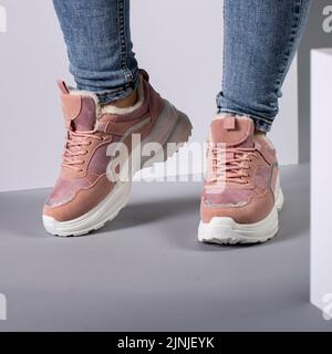 Beschnittenes Bild von warmen rosa Sneakers mit Daunen auf weiblichen Modellbeinen im Studio. Sportschuhe auf den Füßen einer unbekannten jungen Frau, die in Jeans und gekleidet ist Stockfoto