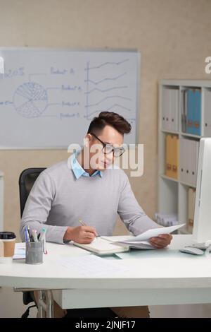 Hübscher junger Geschäftsmann, der Dokument liest und sich Notizen gemacht hat Stockfoto