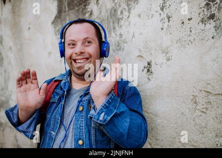 Nahaufnahme eines glücklichen jungen Mannes mit Down Sydrome, der beim Gehen auf der Straße Musik hört. Stockfoto