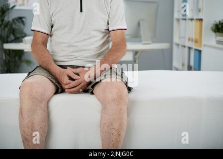 Zugeschnittenes Bild eines alten Mannes, der im medizinischen Büro auf dem Bett sitzt Stockfoto