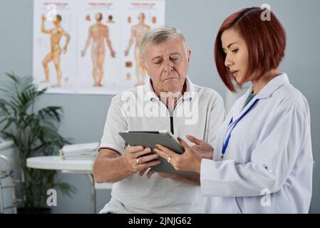 Allgemeinärztin, die den älteren Patienten Analyseergebnisse auf einem Tablet-Computer zeigt Stockfoto