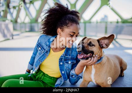 Multirassisches Mädchen, das mit ihrem Hund draußen auf der Brücke sitzt und sich ausruht, ihn trainiert und gemeinsam Freizeit verbringt. Konzept der Beziehung zwischen Stockfoto