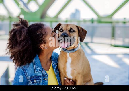 Multirassisches Mädchen, das mit ihrem Hund draußen auf der Brücke sitzt und sich ausruht und gemeinsam Freizeit verbringt. Konzept der Beziehung zwischen Hund und Stockfoto