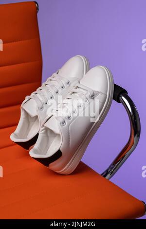 Kreative Werbung. Werbefoto von weißen Sneakers für Frauen oder Teenager auf einem Stuhl im Studio. Nahaufnahme von weißen Sneakers mit schwarzen Einsätzen, die lea im Stehen haben Stockfoto