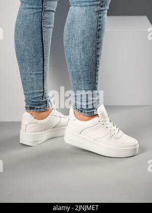 Zugeschnittenes Bild der Seitenansicht des weiblichen Modells von Sportschuhen auf dem Studiohintergrund. Bequeme weiße Sneakers mit Schnürsenkeln an den Beinen eines schlanken, sportlichen Woms Stockfoto