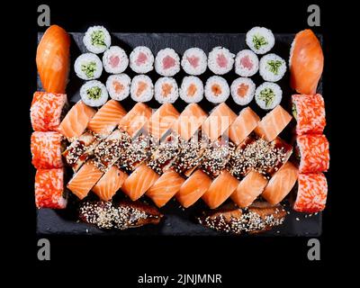 Japanisches Sushi-Essen. Maki und Brötchen mit Thunfisch, Lachs, Garnelen, Krabben und Avocado werden auf Steinschiefer serviert. Draufsicht auf verschiedene Sushi-Sorten. Regenbogen-Sushi Stockfoto