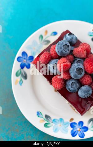 Ein Stück Kuchen mit Mohnsamen und Beerengelee, Kuchen auf einem Teller, der mit saftigen Himbeeren und Heidelbeeren verziert ist Stockfoto