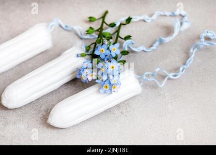 Weibliche Hygiene, Tampons und Vergissmeinnicht-Blüten auf Grau Stockfoto