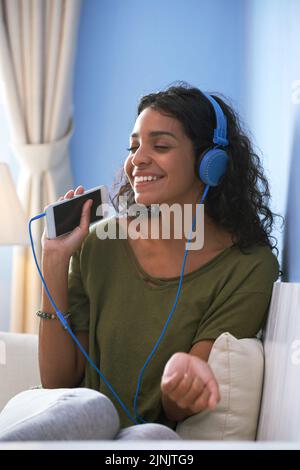 Glückliche, schöne junge Frau, die Musik auf ihrem Smartphone hört Stockfoto