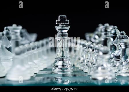Transparente Schachfiguren aus Glas auf dunklem Hintergrund. Führung, Konfrontation und Strategiekonzept Stockfoto