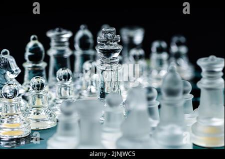 Transparente Schachfiguren aus Glas auf dunklem Hintergrund. Führung, Konfrontation und Strategiekonzept Stockfoto