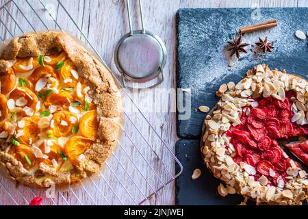 Aprikose- und Erdbeergalette auf Holztisch mit Kochwerkzeugen an der Seite platziert. Stockfoto