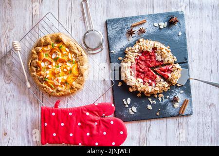 Aprikose- und Erdbeergalette auf Holztisch mit Kochwerkzeugen an der Seite platziert. Stockfoto