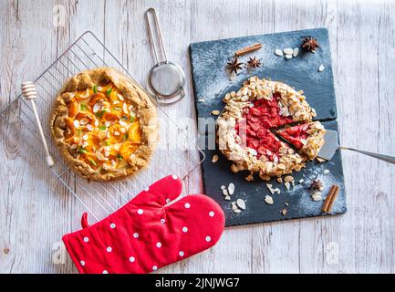 Aprikose- und Erdbeergalette auf Holztisch mit Kochwerkzeugen an der Seite platziert. Stockfoto