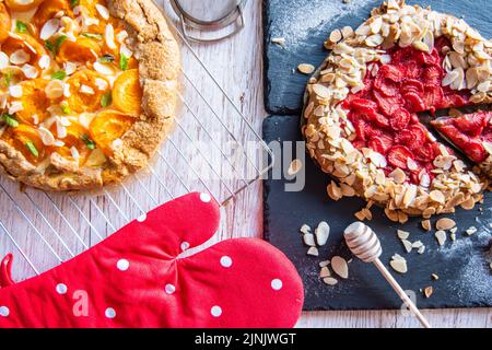 Aprikose- und Erdbeergalette auf Holztisch mit Kochwerkzeugen an der Seite platziert. Stockfoto