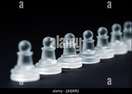 Undurchsichtige Schachfiguren-Reihe aus Glas auf schwarzem Hintergrund, selektiver Fokus, Nahaufnahme Stockfoto