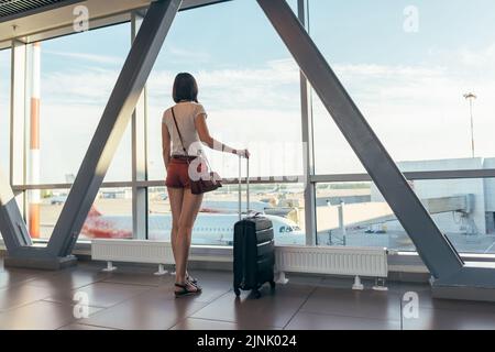 Mädchen auf dem Flughafen in der Nähe der Fenster an den Flugzeugen auf der Start- und Landebahn Stockfoto