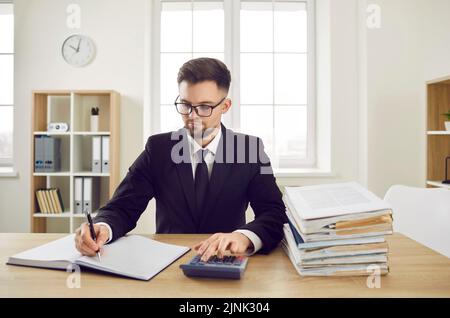 Buchhalter sitzt am Schreibtisch, arbeitet mit Firmendokumenten und verwendet Taschenrechner Stockfoto