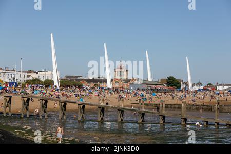 An einem heißen, sonnigen Tag packen viele Touristen den Strand bei Ebbe, im Hintergrund das Kursaal-Gebäude und die Skyline von Southend Beach Stockfoto