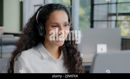 Junge positive Frau mit Kopfhörern kommuniziert über einen Videoanruf-Call-Center-Betreiber spricht mit dem Kunden auf einer Online-Konferenz über eine Webcam am Computer Stockfoto