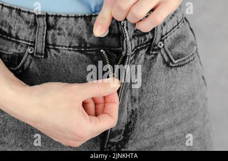 Damenhänden, mit denen Sie Jeans aus nächster Nähe befestigen oder den Flieger entpacken können Stockfoto