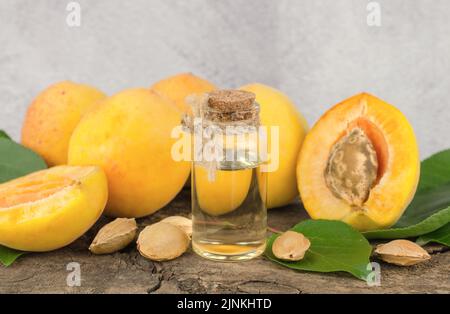 Ätherisches Öl aus Aprikosen- und Aprikosenkernen. Kosmetikflasche mit ätherischem Aprikosenöl und frischen Aprikosenfrüchten auf einem Holztisch Stockfoto