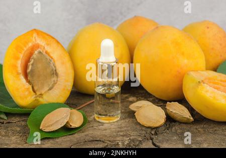 Ätherisches Öl aus Aprikosen- und Aprikosenkernen. Kosmetikflasche mit ätherischem Aprikosenöl und frischen Aprikosenfrüchten auf einem Holztisch Stockfoto