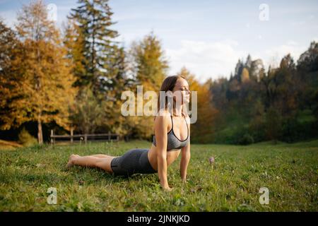 Junge Frau in Sportkleidung, die Yoga und Meditation praktiziert und Atemübungen im Freien macht.