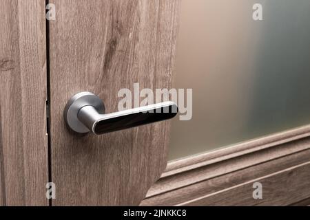 Nahaufnahme des Türgriffs aus Stahl an der braunen Holztür. Stockfoto