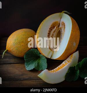 Frische ganze und geschnitten von japanischen Melonen, Honigmelone Cantaloupe (Cucumis melo) Blatt Holztisch Hintergrund. Obst Sommer Früchte Gesundheitskonzept. Stockfoto