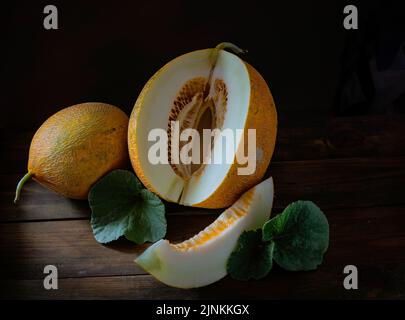 Frische ganze und geschnitten von japanischen Melonen, Honigmelone Cantaloupe (Cucumis melo) Blatt Holztisch Hintergrund. Obst Sommer Früchte Gesundheitskonzept. Stockfoto