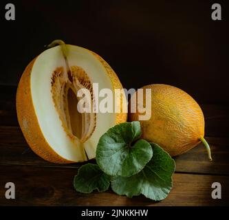 Frische ganze und geschnitten von japanischen Melonen, Honigmelone Cantaloupe (Cucumis melo) Blatt Holztisch Hintergrund. Obst Sommer Früchte Gesundheitskonzept. Stockfoto