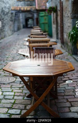 Holztische und -Stühle in einer gepflasterten Gasse im Vintage-Look. Stockfoto