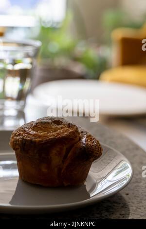 Pfannkuchen oder Cupcake auf Keramikplatte, Terrazzo-Tisch, im Hintergrund aus Sesseln und Glas Wasser Stockfoto