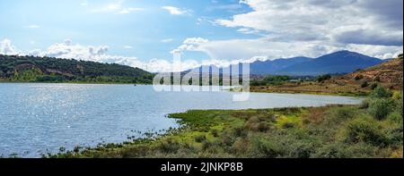 Panorama-Berglandschaft mit großem sonnigen See und kleiner Stadt am Ufer. Stockfoto