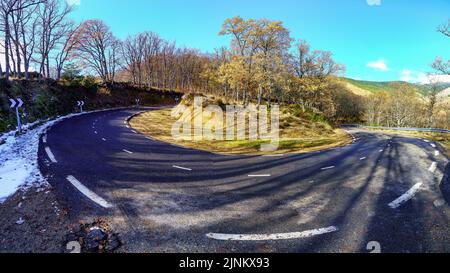 Sehr scharfe Kurve der Bergstraße zwischen Bäumen und Schnee auf dem Asphalt. Guadarrama Madrid. Stockfoto