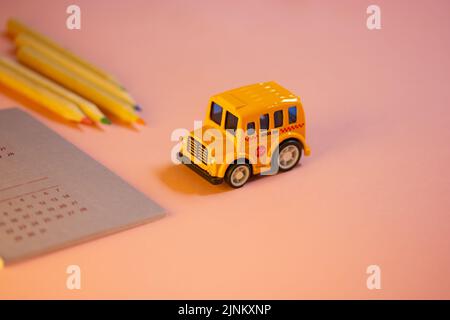 Spielzeug gelb amerikanischen Schulbus auf Tisch, Kalender mit Daten, bunte Holzstifte liegen auf rosa Tisch. Schreibwaren für Studium, Zeichnung, Planung. Stockfoto